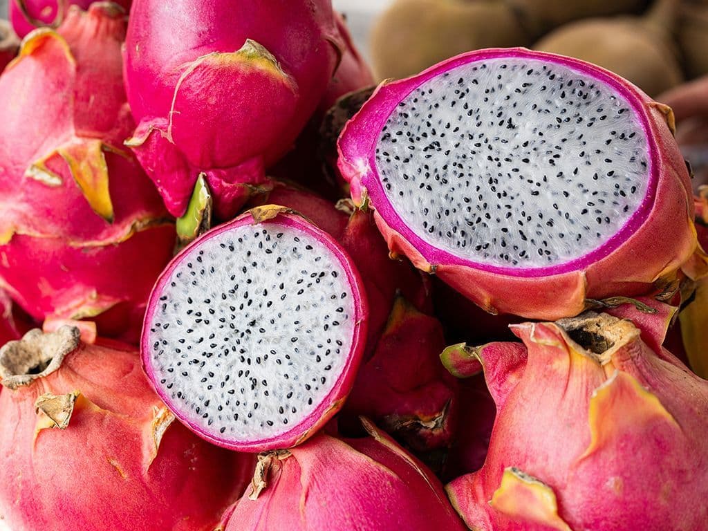 Welke felroze vrucht van een cactusplant heeft uitstekende, groene schubben aan de buitenkant en bevat zacht, wit vruchtvlees vol met kleine, zwarte, eetbare pitjes?