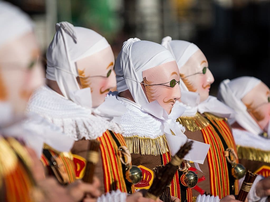 Rond diezelfde periode, op Vastenavond, de dag voor Aswoensdag gaan ook in Henegouwen enkele festiviteiten door. De festiviteiten draaien daar vaak rond anonieme folkloristische personages, met masker, hoed met struisvogelveren, een riem met bellen, klompen en korf met sinaasappels die enkel mogen gedragen worden door mannen. Hoe heet dit anoniem folkloristische personage dat in verschillende Waalse steden wordt opgevoerd?