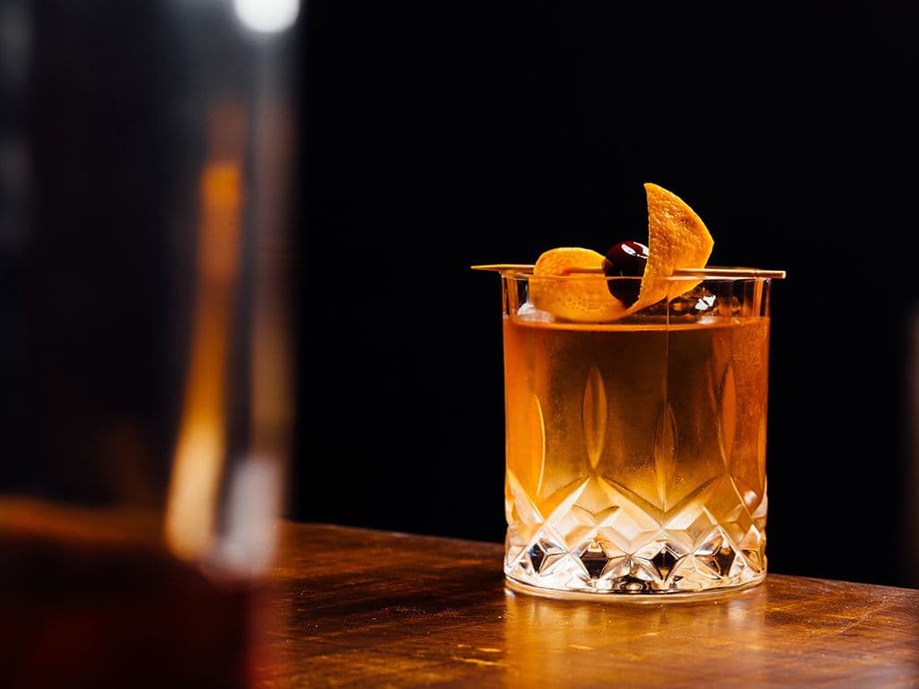 Een cocktail smaakt altijd! Maar nog meer als er wat geschiedenis achter schuilt want dit is één van de oudste cocktailrecepten die gedocumenteerd is. De bereiding is als volgt: we beginnen met een suikerklontje, daarop komen twee scheutjes Angostura bitters en samen worden ze geplet met een muddler. Ijsblokjes, sodawater, bourbon of whisky en een gekonfijte kers maken het geheel dan af. Hoe heet deze cocktail die ondanks zijn “leeftijd” tot op vandaag nog altijd heel populair is?
