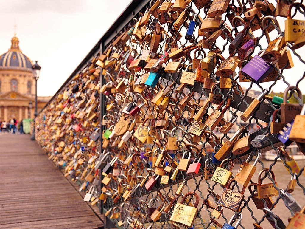Welke iconische Parijse voetgangersbrug over de Seine werd wereldwijd bekend door de traditie waarbij koppels een hangslot aan de relingen bevestigden als symbool van hun eeuwige liefde, en de sleutel in de rivier gooiden? Deze traditie begon in 2008, maar werd in 2014 stopgezet door de vervanging van de relingen. De brug verbindt het Collège des Quatre-Nations met het Louvre en is een geliefde plek voor toeristen. Met een lengte van 155 meter en een breedte van 11 meter biedt deze brug een prachtig uitzicht op de stad. Wat is de naam van deze beroemde brug?