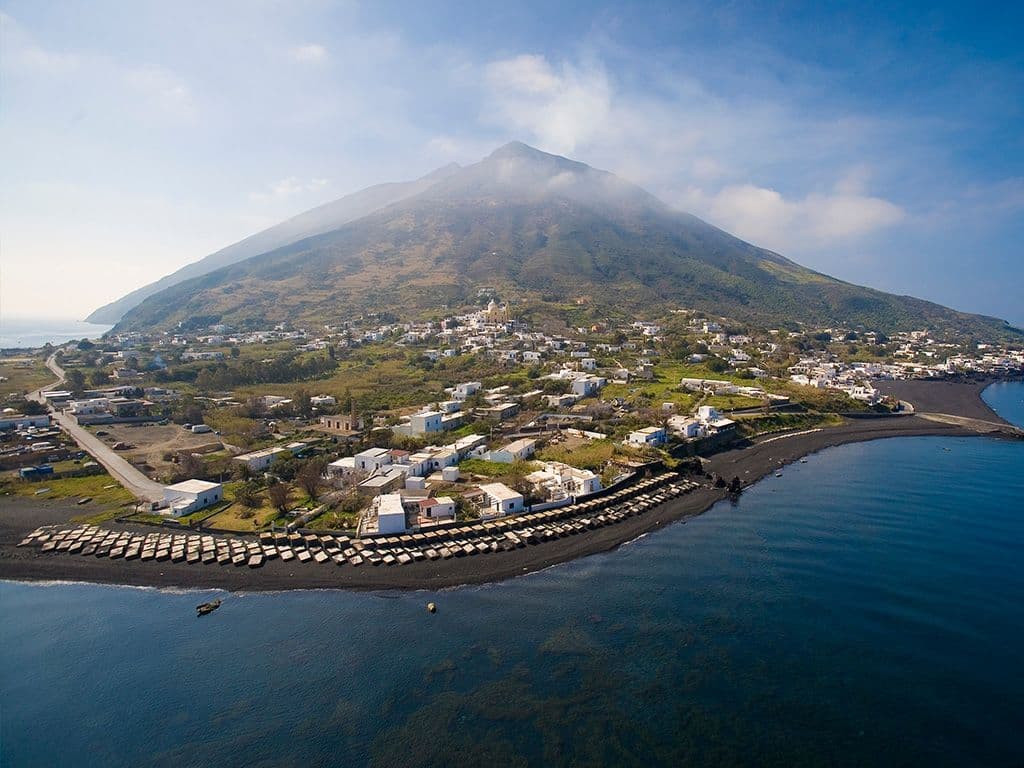 We zien hier een foto van een dorp dat in 79 na christus met een laag van 4m as en lava bedekt werd na de uitbarsting van een vulkaan. U weet uiteraard dat dit Pompeii is en dat de boosdoener op de achtergrond de Vesuvius is. Bij diezelfde uitbarsting werd nog een ander dorp verwoest. Als fervent kwisser weet u dat het om Herkulaneum gaat. Er zijn echter nog steeds vulkanen actief in Italië. We zijn op zoek naar een actieve vulkaan die een vulkaaneiland vormt in de Tyrreense Zee. Deze vulkaan gaf zijn naam trouwens een het type uitbarsting waarbij blokken en vulkanische bommen uit de vulkaan omhoog gegooid worden en op de omgeving neervallen. Maar de naam is ook bekend door een opgevulde en opgerolde pizza. Zijn naam.